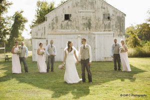 bride and groom and wedding party by rustic barn